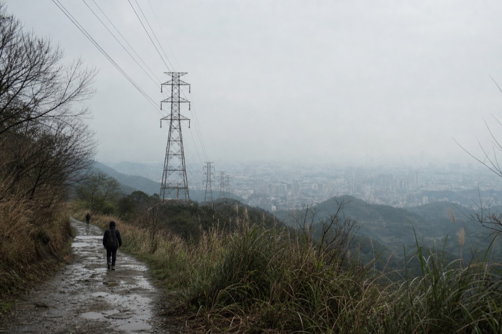 Cable car towers standing on a forested ridge in Taiwan with the Taipei basin in the distance, no text, no logos, no people