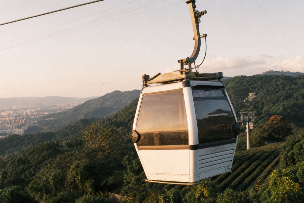Close view of a gondola cabin suspended from a cable above green hills, no text, no logos, no people