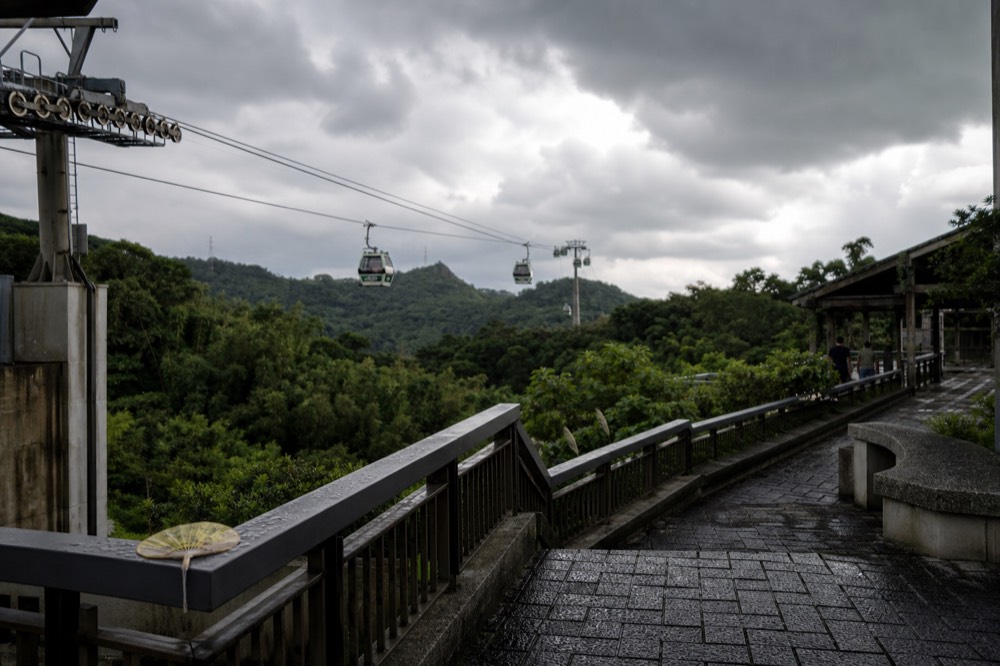 Gondola cabins on the cable under a cloudy sky above Taipei hills, no text, no logos, no people