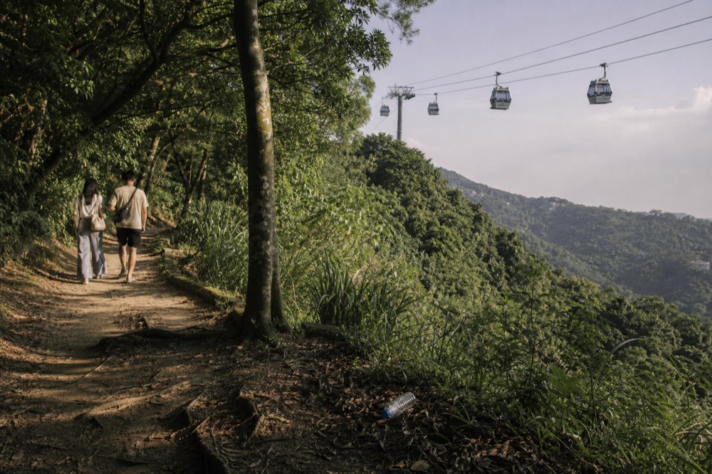 Gondola cabins travelling on a long cable line above forested hills near Taipei, no text, no logos, no people