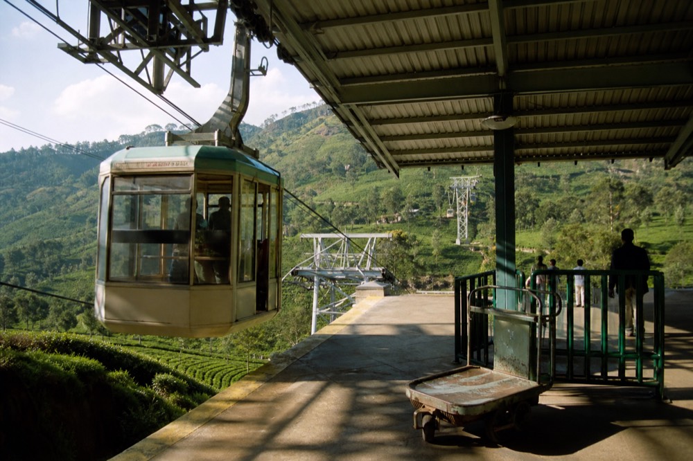 Gondola cabins arriving at a hillside station above tea country, no text, no logos, no people