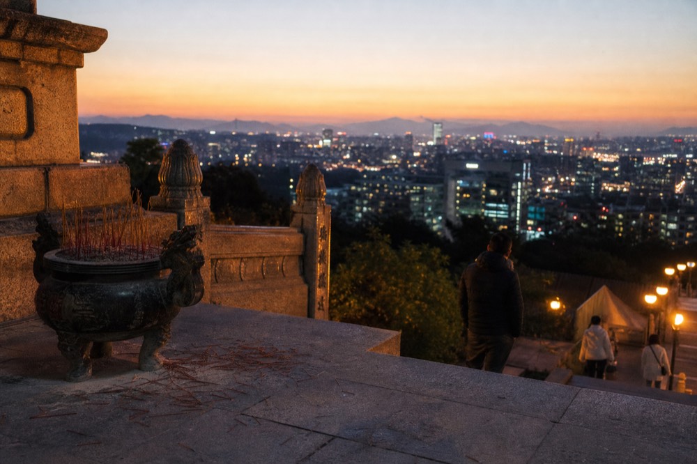 A stone temple forecourt overlooking a wide city basin at dusk, no text, no logos, no people