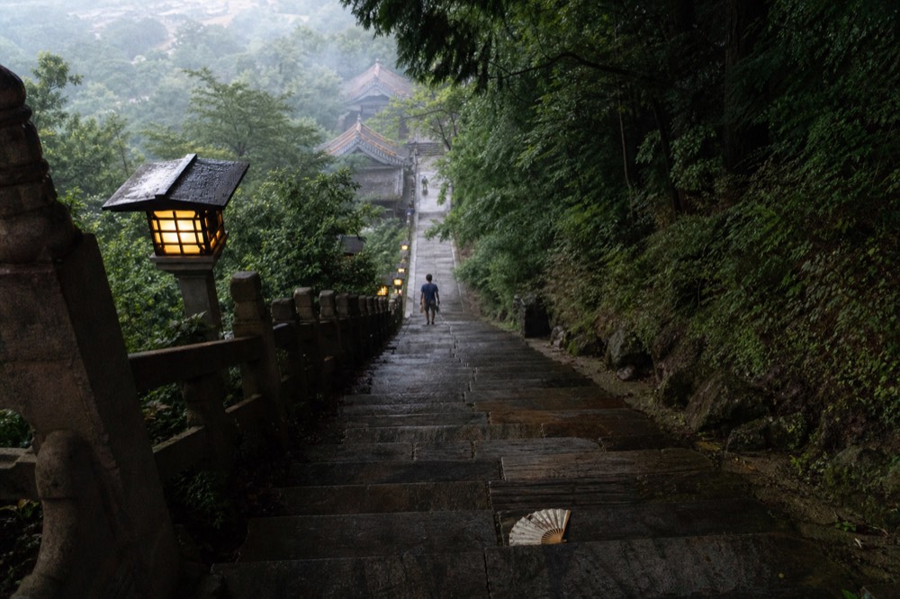 A long stone staircase with lanterns rising through forest to a temple, no text, no logos, no people
