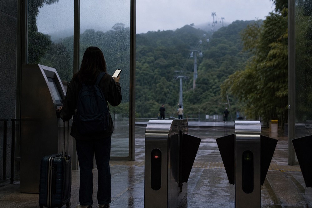 A traveler holding a phone at a gondola station turnstile, no text, no logos, no people